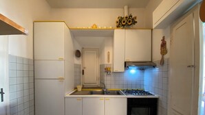 Pieni, käytännöllinen keittiö, jossa on valkoiset kaapit, liesi ja pesuallas.