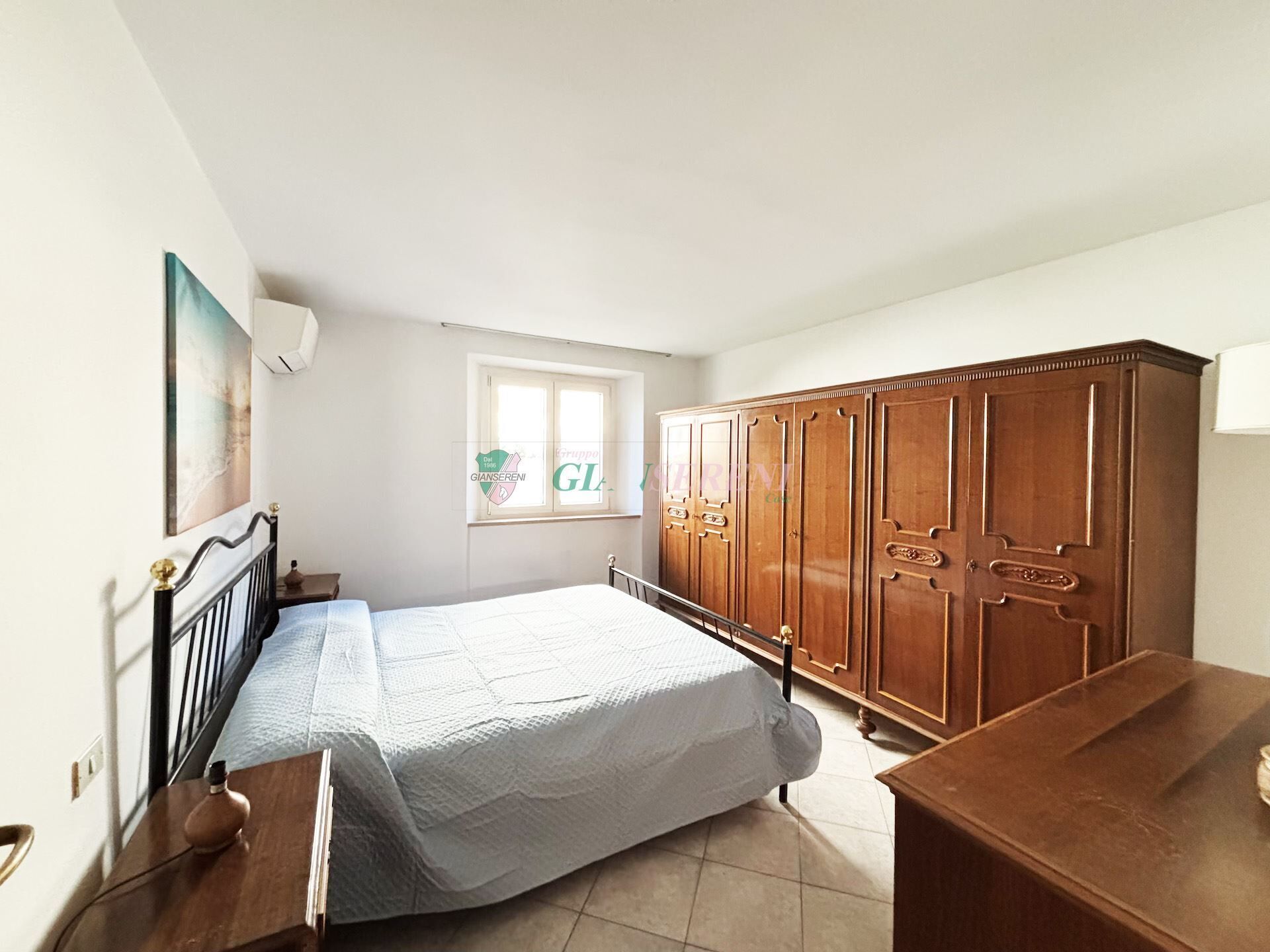 A bedroom with a bed, wooden wardrobe, and a window with a view of the garden.