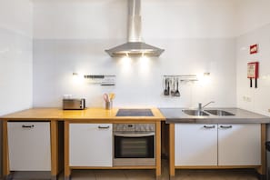 A modern kitchen with white cabinets, a stainless steel range hood, a built-in oven, and a double sink.