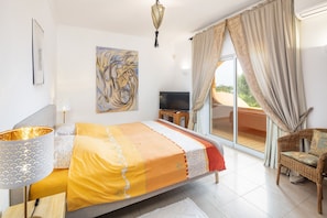Quarto com cama, televisão, pintura e varanda com cortinas.