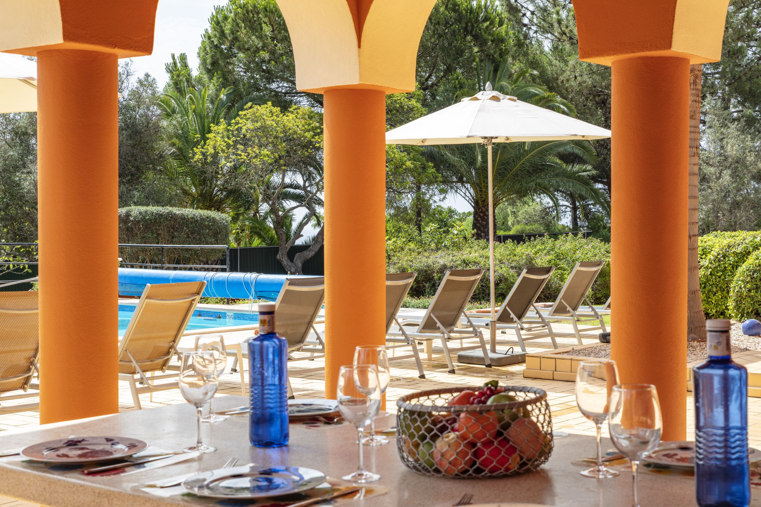 Un espace repas aménagé au bord de la piscine, avec des tables, des chaises et des parasols.