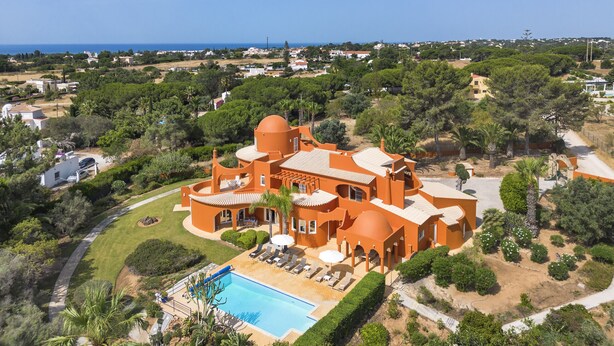 Een ruime, oranje villa met zwembad, omgeven door weelderige begroeiing en uitzicht op zee.