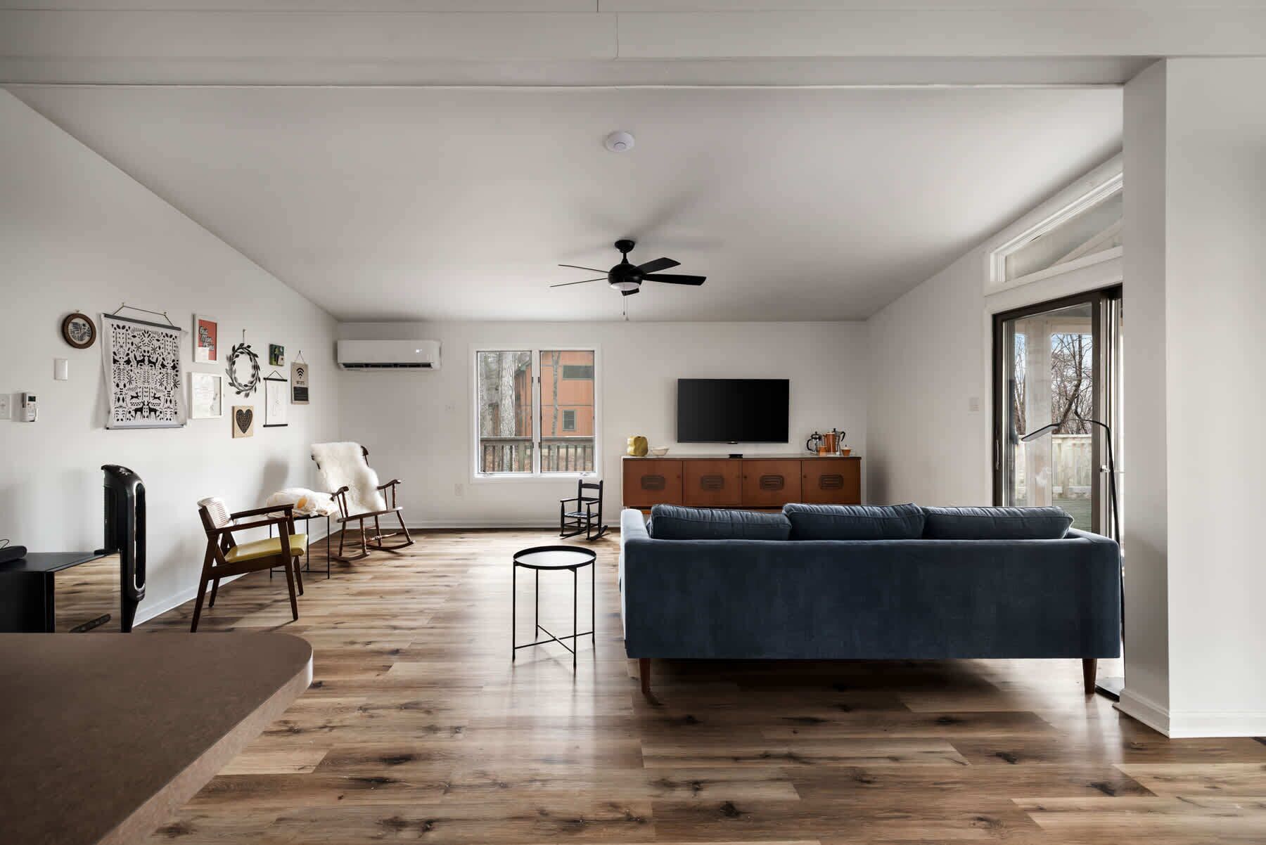 Una sala de estar moderna con un sofá azul, suelo de madera y un televisor en la pared.