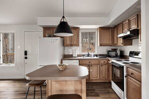A modern kitchen with wooden cabinets, a white refrigerator, a stove, a microwave, and a hanging pendant light. - Cozy cabin w/deck & grill, dog-friendly, trails (Berkeley Springs)