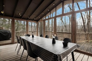 A covered outdoor dining area with a long table, chairs, and a grill.