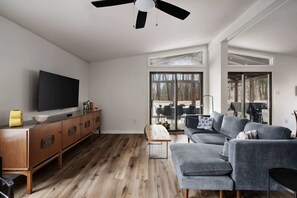A modern living room with a flat-screen TV, wooden cabinet, grey sofa, and a ceiling fan. - Cozy cabin w/deck & grill, dog-friendly, trails (Berkeley Springs)