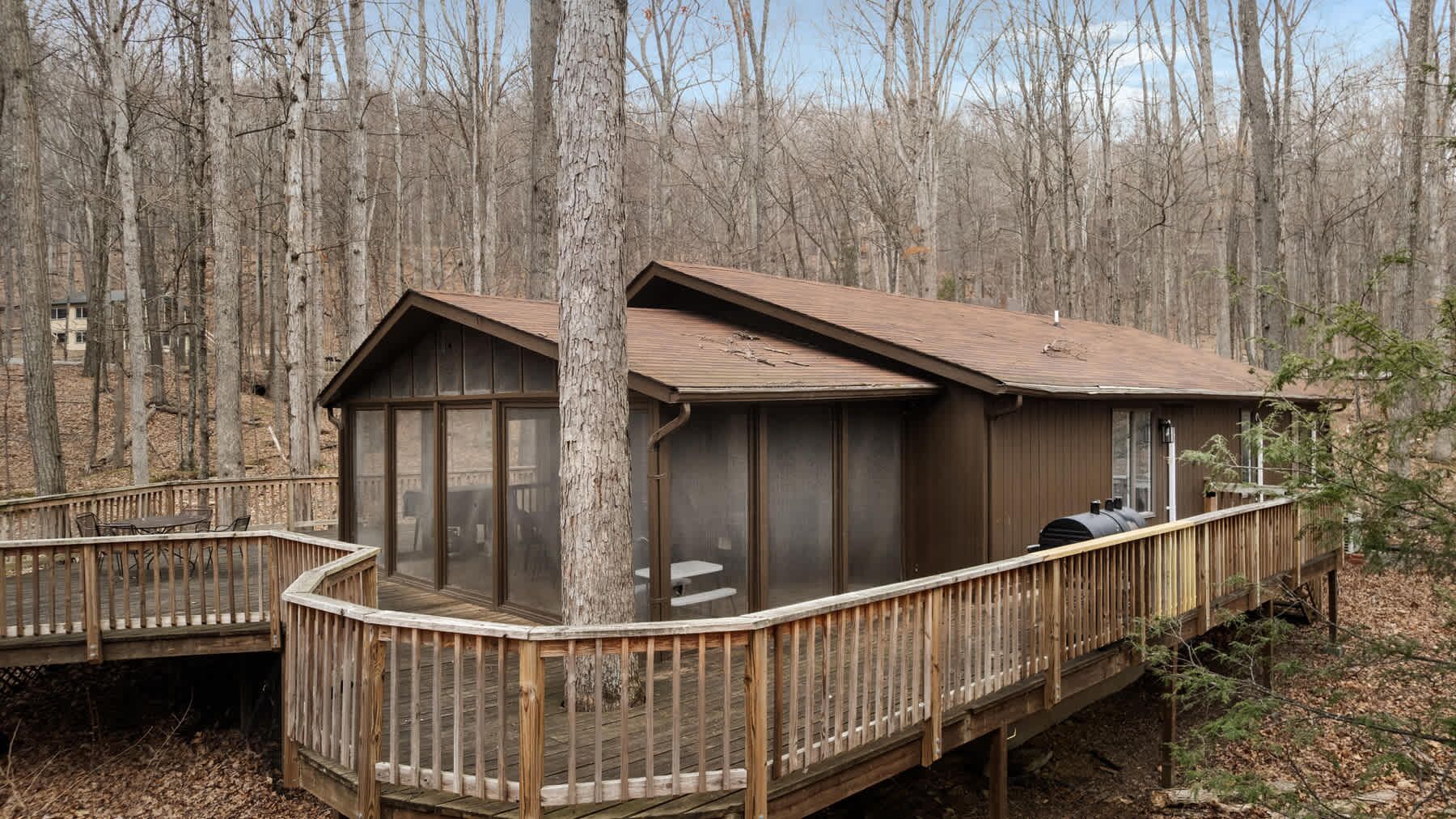 A cabin with a deck, large windows, and a chimney.