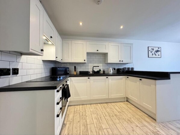 A modern kitchen with white cabinets, black countertops, and a wooden floor. - 4 Guests - 2 Bedrooms - Parking - 9min City Centre (Doncaster)