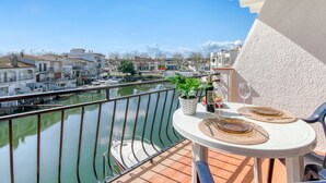 Un balcon avec une table dressée pour deux personnes, donnant sur un canal où naviguent des bateaux.