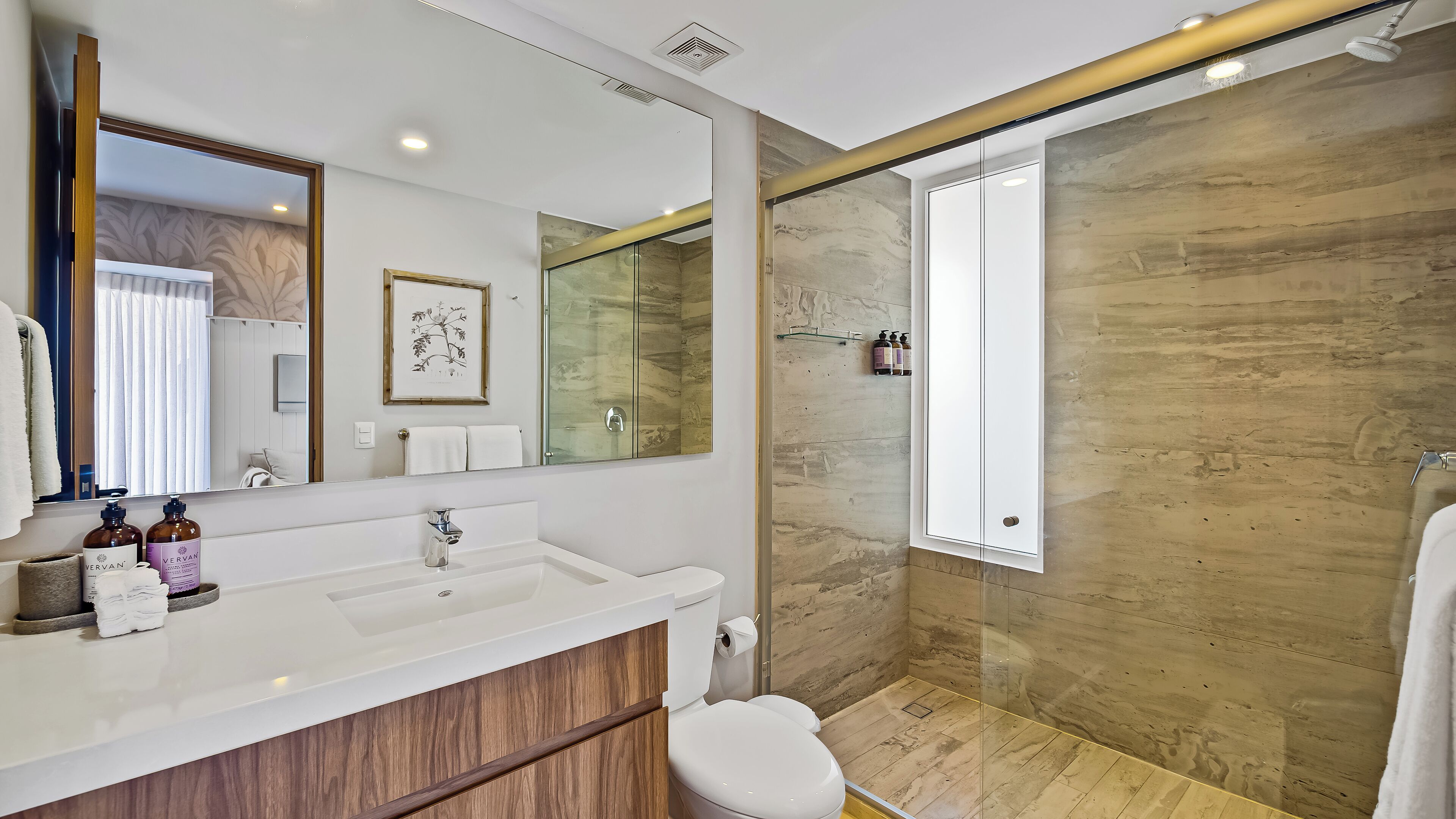 A modern bathroom with a white vanity, a large mirror, a shower with a glass door, and a wooden floor.