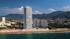 A coastal cityscape with high-rise buildings, a beach, and mountains in the background.