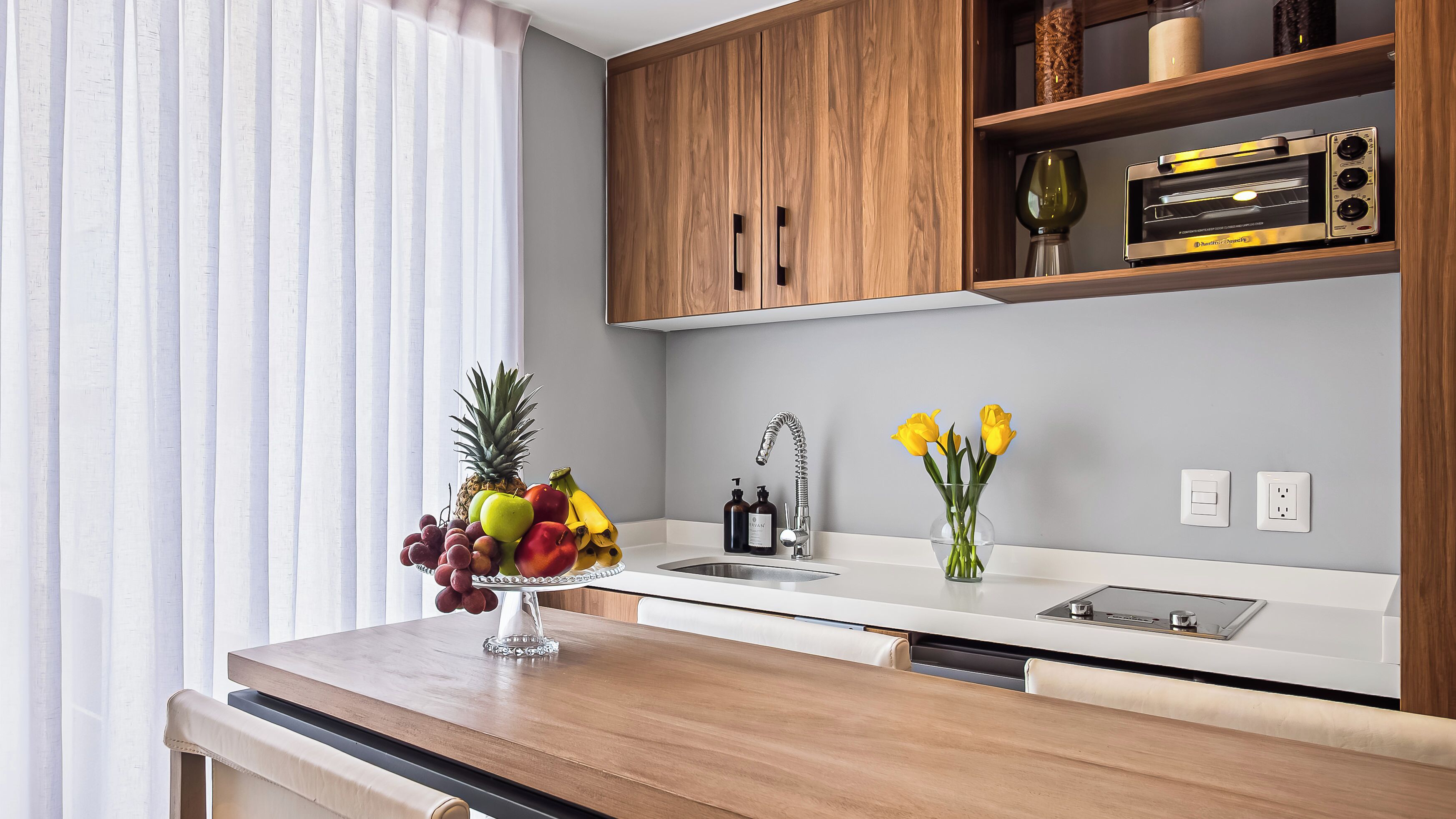 Une cuisine moderne avec des meubles en bois, un évier en acier inoxydable et un panier de fruits posé sur le plan de travail.