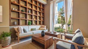 A living room with a wooden bookshelf, a sofa, a coffee table, and a view of the outdoors through large windows.