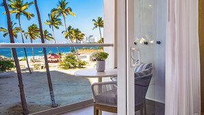 A balcony with a view of the beach, palm trees, and a cityscape.