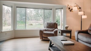 A modern living room with a large bay window, a leather armchair, a wooden coffee table, and a floor lamp.