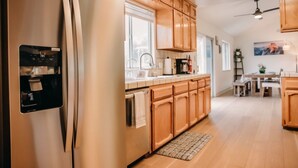 A modern kitchen with wooden cabinets, a stainless steel refrigerator, a built-in water dispenser, and a dining area with a table and chairs.
