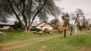 A house with a garage, surrounded by trees and a dirt path.