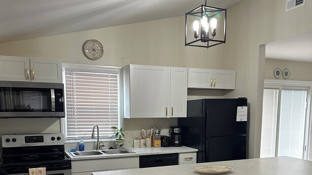A modern kitchen with white cabinetry, a black refrigerator, a built-in oven, a microwave, and a bar area with stools.