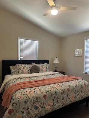 A bedroom with a bed, a ceiling fan, a nightstand, a lamp, and a wall-mounted picture.