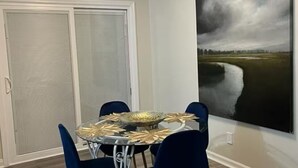 A dining area with a round table, blue chairs, and a large landscape painting on the wall.