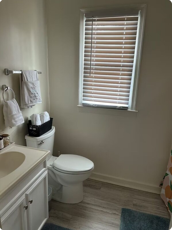 A bathroom with a toilet, a sink, a window with blinds, and a towel rack with multiple towels.