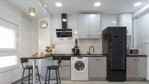 Una cocina moderna con armarios blancos, un refrigerador negro, una lavadora y un comedor con dos taburetes.