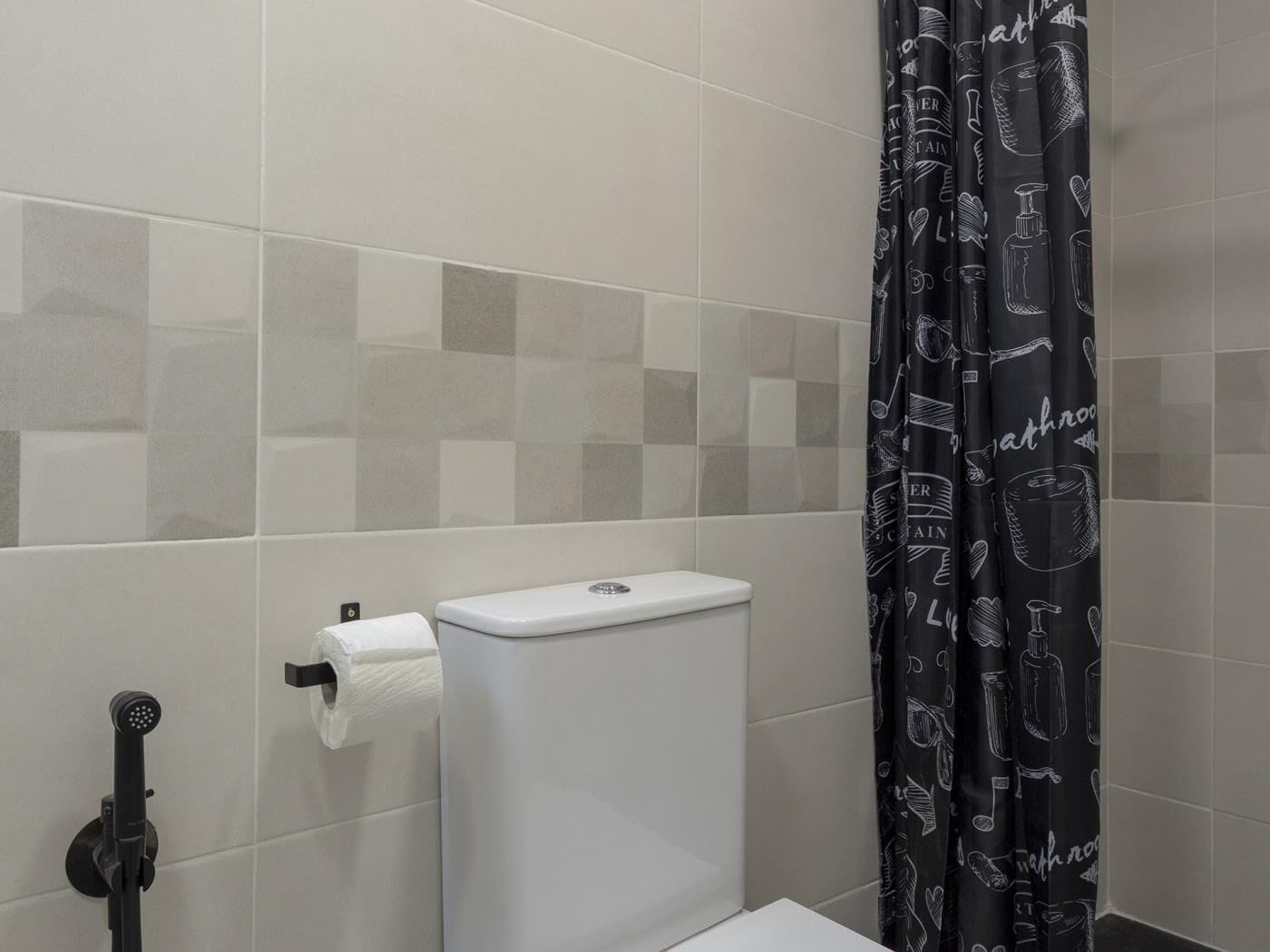 Un bagno con il water, un rotolo di carta igienica, un soffione della doccia e una tenda da doccia nera con illustrazioni a tema bagno.