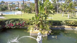 A landscaped area with a water feature, palm trees, and a building in the background.