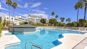 A swimming pool with a tiled deck, a small gazebo, and palm trees.
