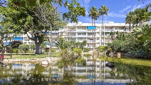 Un hotel con varios pisos, piscina y abundante vegetación.
