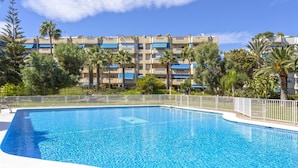 Una piscina con una cerca blanca, rodeada de palmeras y un edificio de varios pisos con balcones.