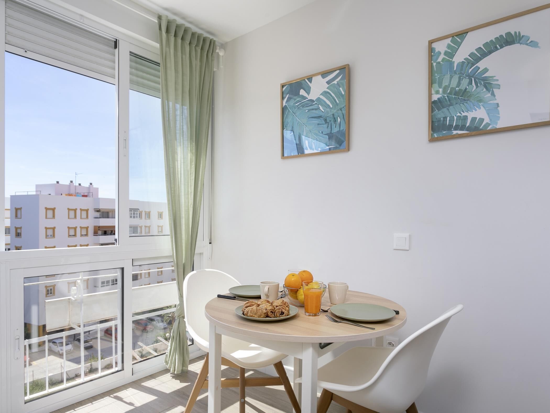 Een balkon met een ontbijttafel, uitzicht op de stad en twee ingelijste kunstwerken aan de muur.