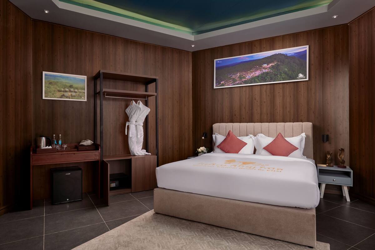 A modern hotel room with a large bed, wooden panel walls, a small desk, and a wardrobe.