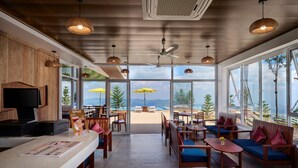 A modern interior with wooden paneling, a reception desk, and seating areas with a view of the beach and mountains.