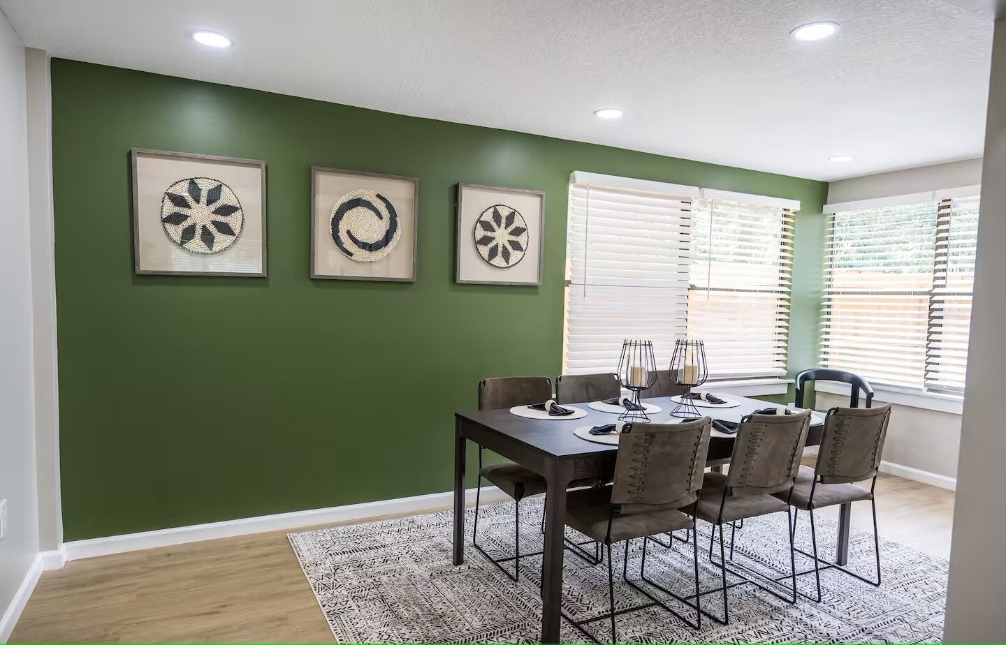 A dining area with a green wall, three framed wall art pieces, a dark wooden table, and six chairs.