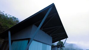 A modern building with a sloped roof and large windows, surrounded by lush greenery and misty mountains. - Noah Crest (Kodaikanal)