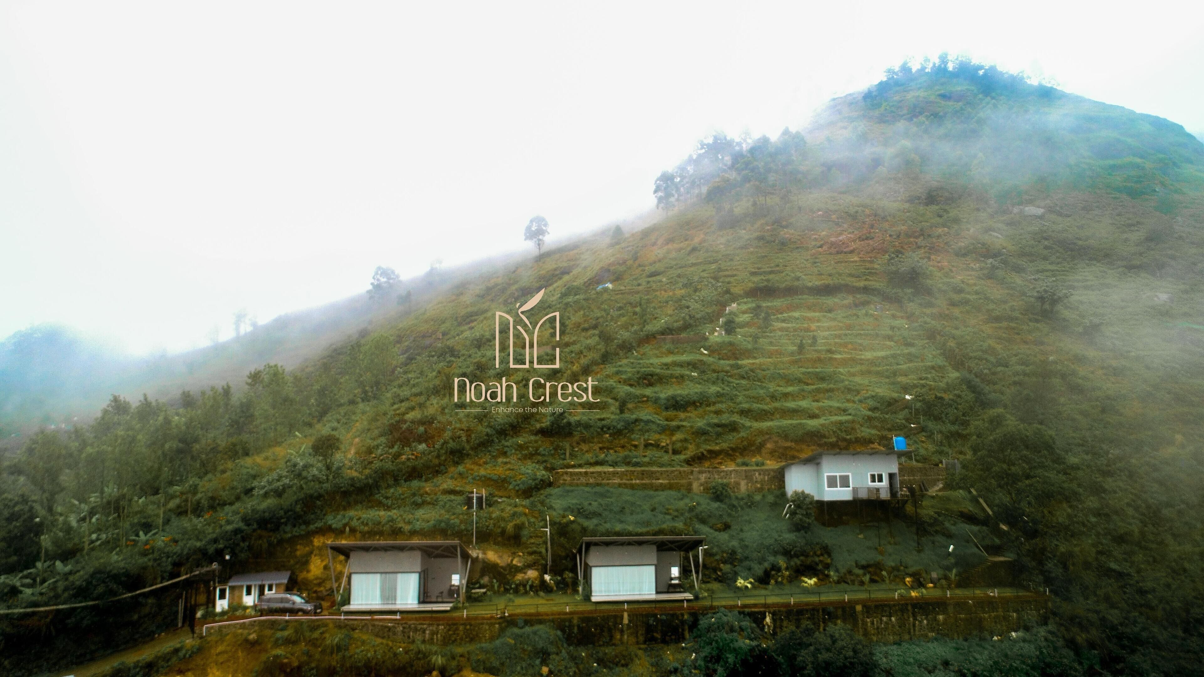 Una ladera con casas modernas y minimalistas, una vista despejada de la naturaleza circundante y el logo de 'Noah Crest' en el centro.