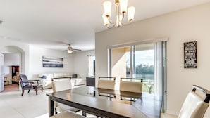 Amplia sala de estar con una gran mesa de comedor, asientos cómodos, un ventilador de techo y vistas a través de una puerta corrediza de vidrio.