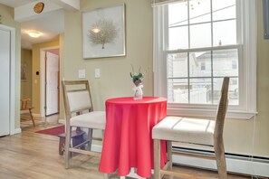 A room with a round table covered in a red tablecloth, two chairs, a vase with flowers, a framed picture on the wall, and a window with a view of a house. - Near Beaches & Waterfront Dining: Home in Hampton! (Hampton)