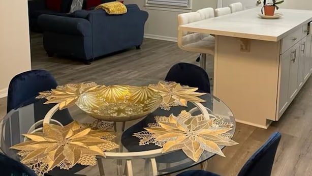 Un comedor con mesa de vidrio, sillas azules y hojas doradas decorativas.