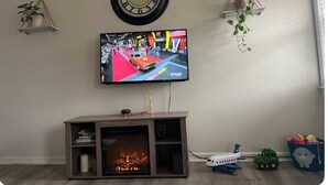 Una sala de estar con televisor de pantalla plana, chimenea, reloj y juguetes infantiles.