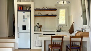 A modern kitchen with a refrigerator, wooden shelves, and a dining area with striped cushions.