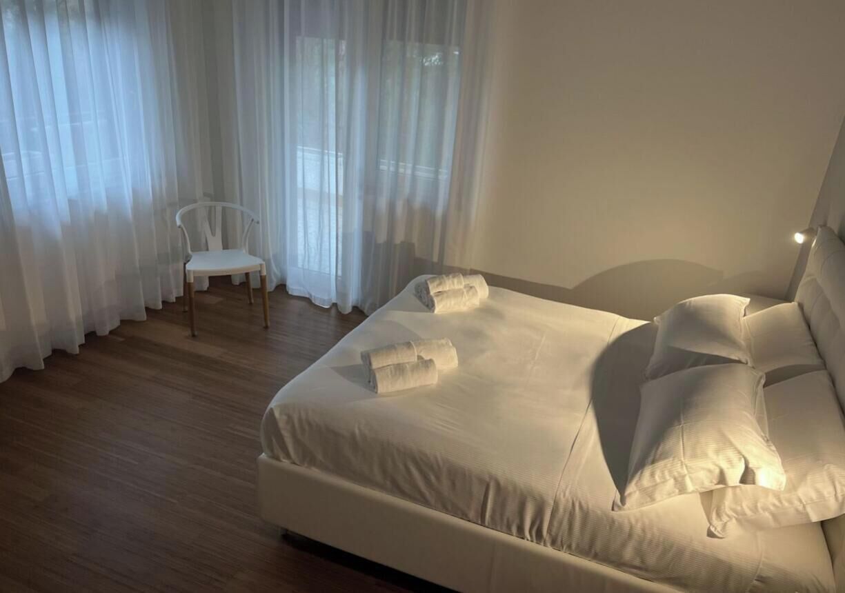 Un dormitorio con cama, una silla y cortinas translúcidas.