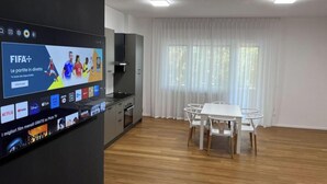 A modern living room with a flat-screen TV, a dining table, and a kitchen area. - Villa Riviera 287 - Appartamento Mare (Pescara)
