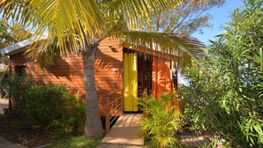 A wooden cabin with a yellow door, surrounded by lush greenery and a palm tree. - Direct Privilege Rate - 2 adults (Saint-Paul)