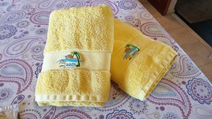 Two yellow towels with embroidered logos on a patterned bedspread. - Direct Privilege Rate - 2 adults (Saint-Paul)
