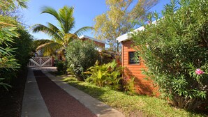 A pathway leading to a building with a red exterior, surrounded by lush greenery and palm trees. - Direct Privilege Rate - 2 adults (Saint-Paul)