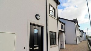 A row of modern, single-story houses with a uniform facade, featuring a black front door with the number 2, a small window above the door, and a white panel on the wall to the left. - Charming 2-Bed Apartment in Dublin's Countryside (Ballyboughal)
