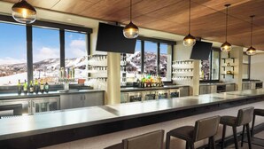 A bar area with a long counter, multiple bar stools, and a view of a snowy mountain landscape through large windows.