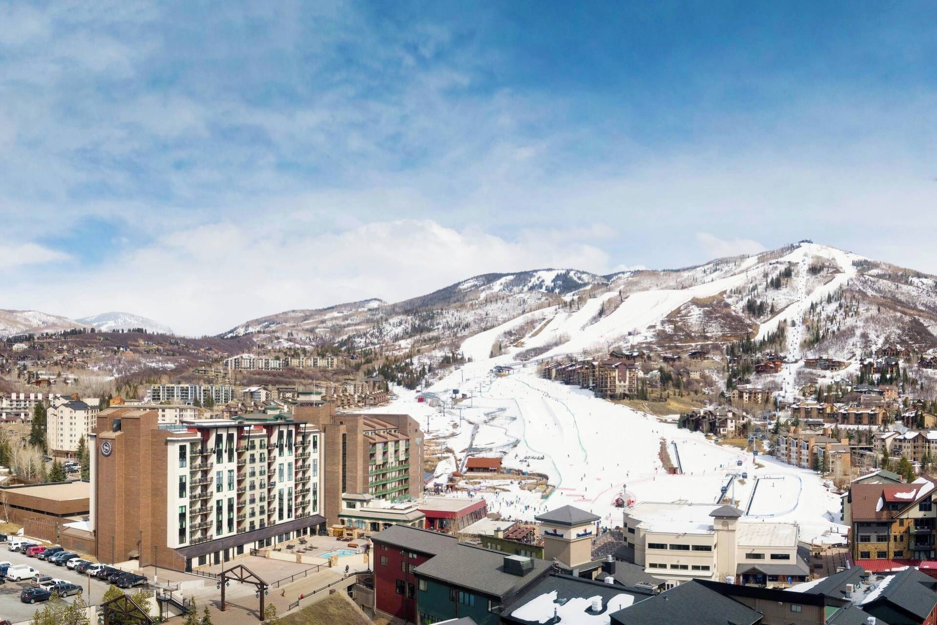 A ski resort with multiple buildings, including a hotel with a pool area and a ski lift visible in the background.